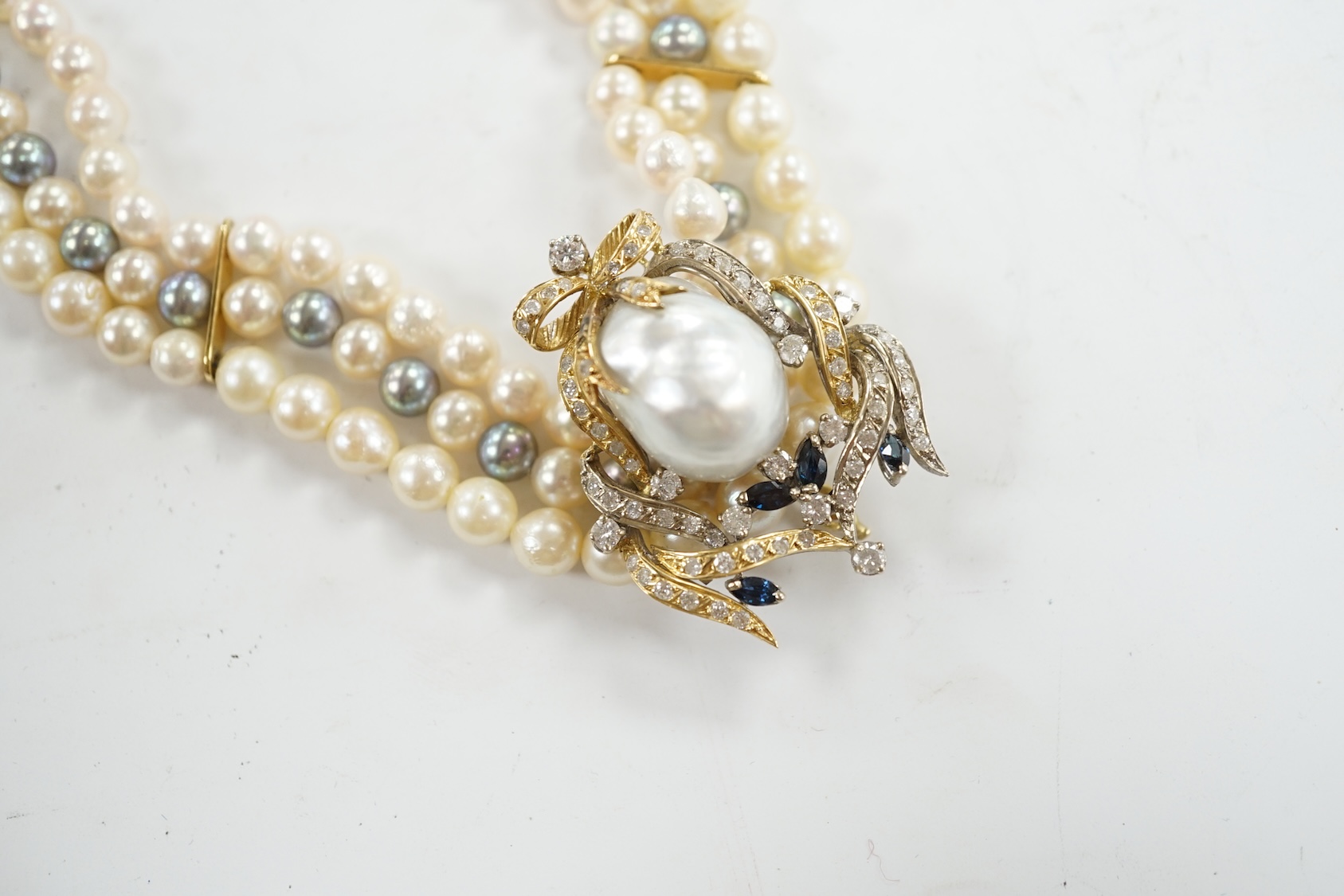 A modern triple strand two colour cultured pearl necklace, with yellow metal clasp and detachable yellow metal baroque pearl, sapphire and diamond cluster set clip, 43cm, gross weight 101.9 grams. Condition - fair to goo